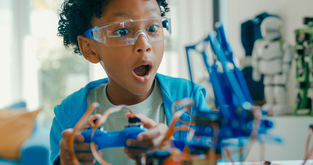 A young African American boy wearing safety goggles looking surprised at a science experiment