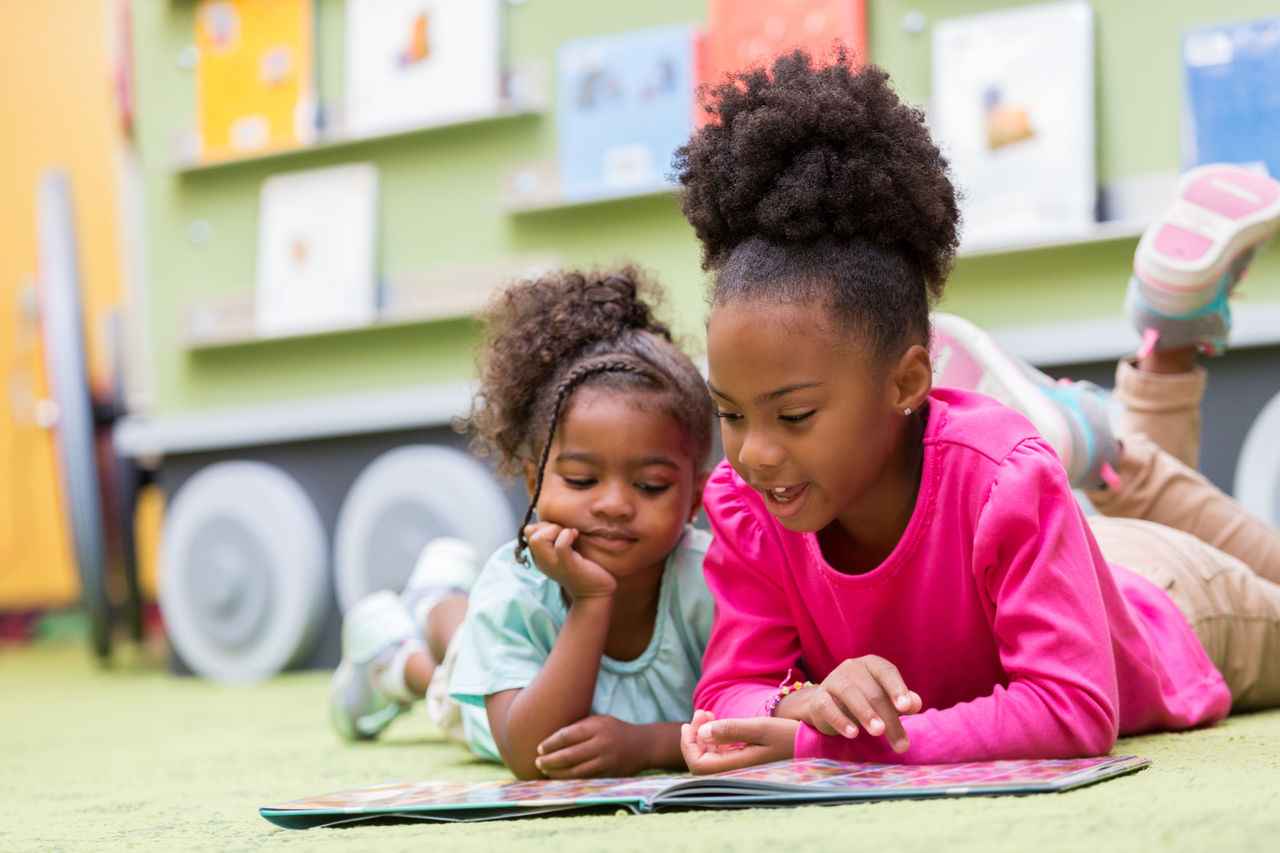 Two African American girls lying on the floor reading a book together