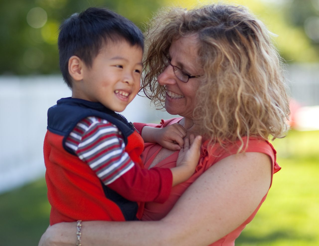 A mother holds her smiling young son outside.